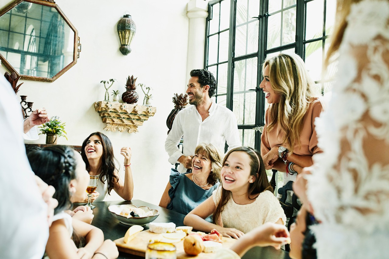Family diner laughing Laughing multigenerational family gathered around dining room table sharing appetizers before birthday dinner