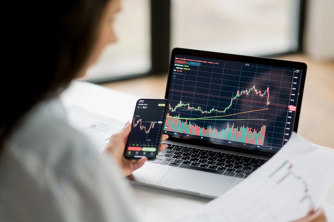 Computer phone dashboard Successful smart woman investor and crypto trader, using laptop and smartphone, analyzes charts of trading in stock market and digital cryptocurrency exchange, conducts analysis, trading crypto coins