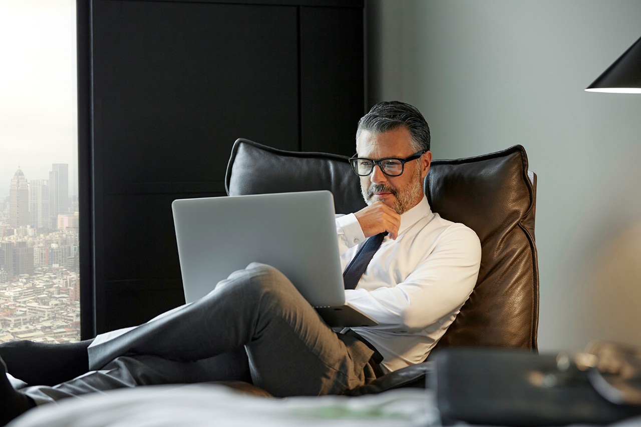 Man looking computer Full length of thoughtful businessman using laptop in hotel room. Professional is working. He is wearing eyeglasses.